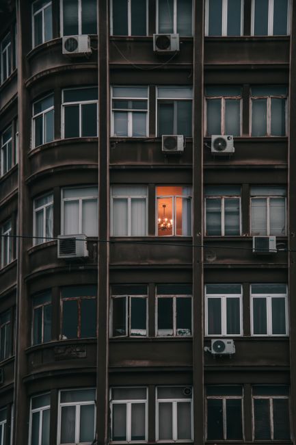 A city apartment building facade with one lit window, showcasing urban contrasts.