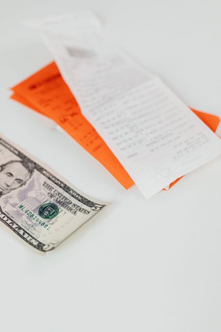 A close-up of a five-dollar bill and receipts on a white background, symbolizing finance and expenses.