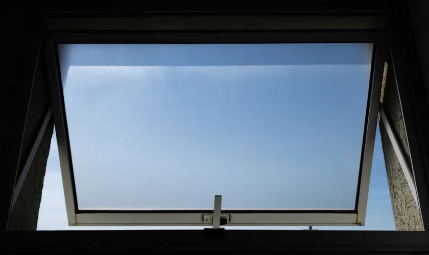 A low angle view of an open skylight window revealing a clear blue sky.
