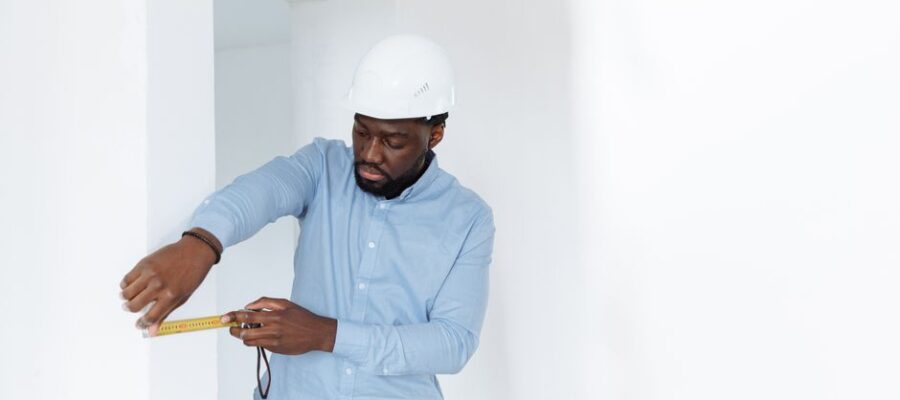 A man in a hard hat measures a wall, showcasing precision in a building interior.