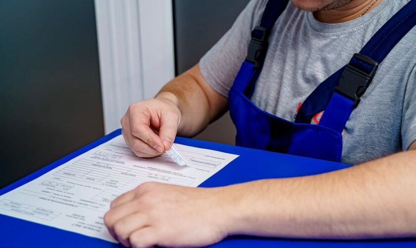 A mechanic in overalls reviews paperwork at a desk in an office setting.