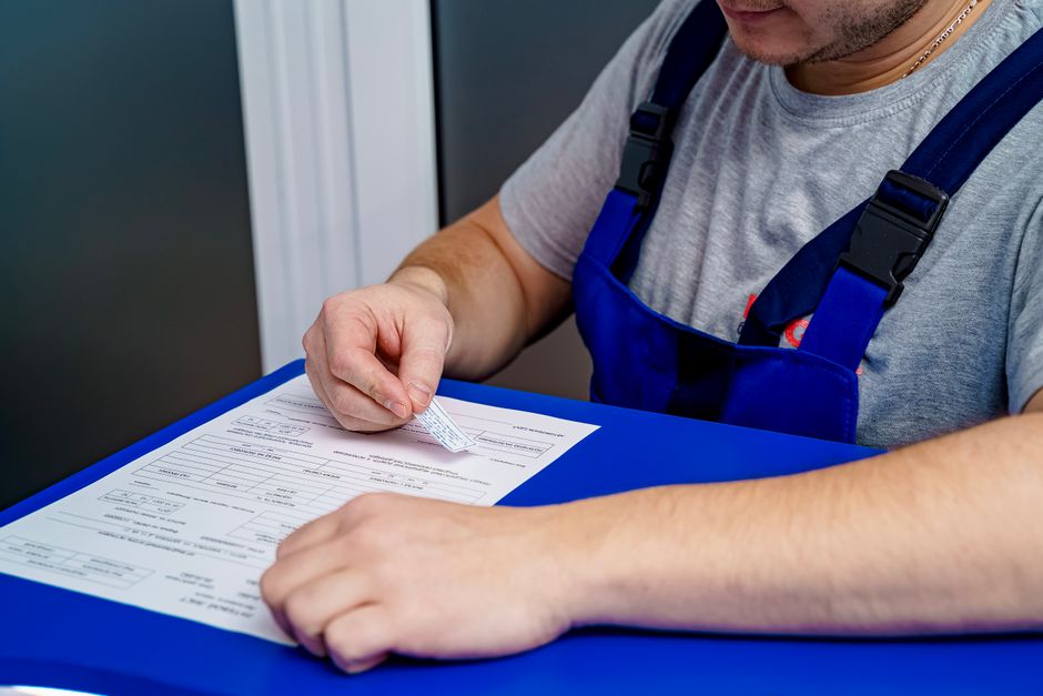 A mechanic in overalls reviews paperwork at a desk in an office setting.