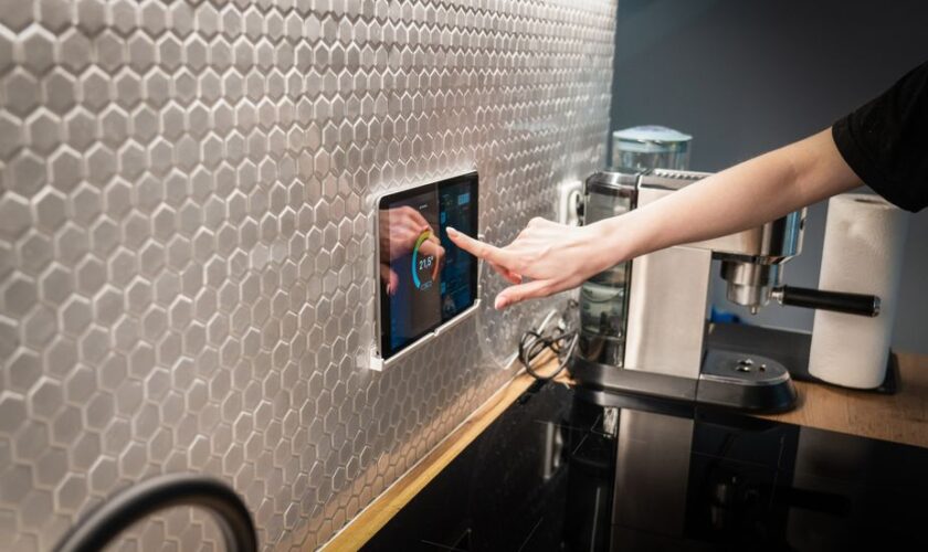 A modern kitchen with a touchscreen smart home control panel integrated into a hexagon-patterned wall.