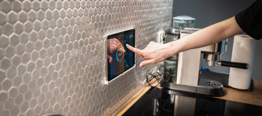 A modern kitchen with a touchscreen smart home control panel integrated into a hexagon-patterned wall.