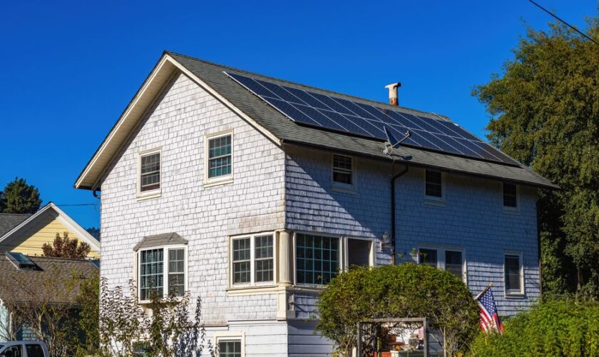 A modern two-story home with solar panels on its roof under a clear blue sky.