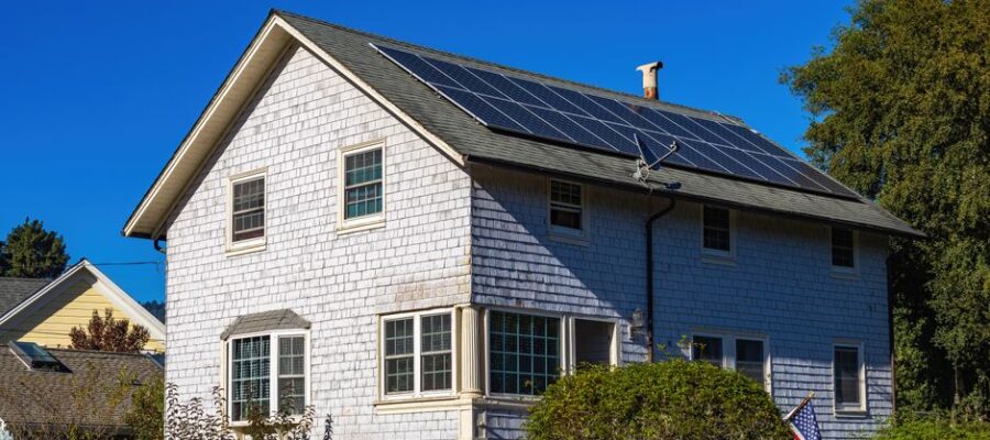 A modern two-story home with solar panels on its roof under a clear blue sky.
