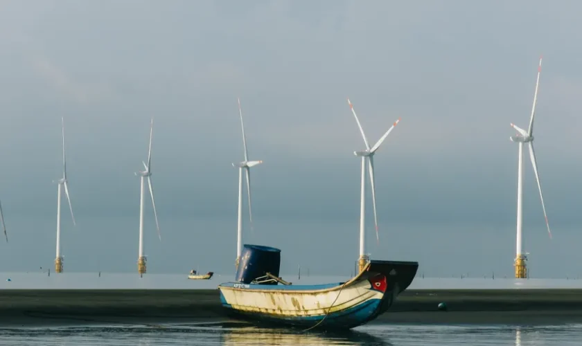A peaceful coastal scene with a fishing boat and wind turbines on a calm sea.
