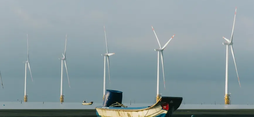 A peaceful coastal scene with a fishing boat and wind turbines on a calm sea.