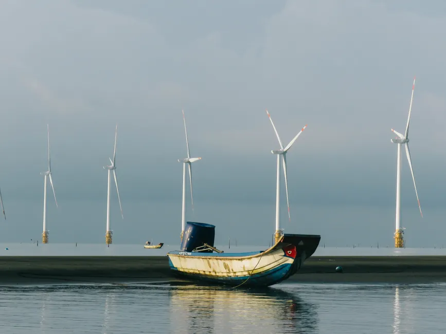 A peaceful coastal scene with a fishing boat and wind turbines on a calm sea.