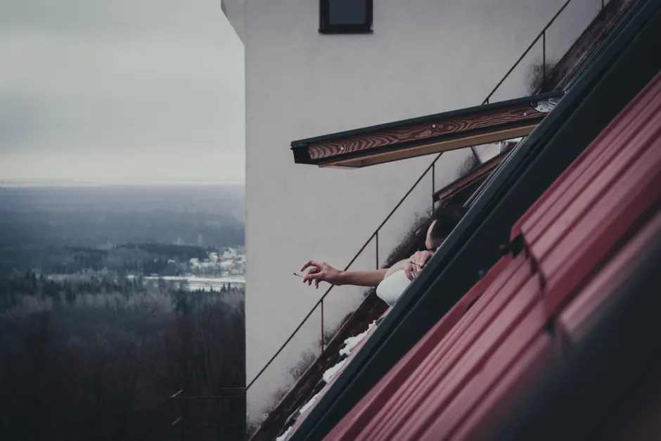 A person reaching out from an attic window overlooking a winter landscape.