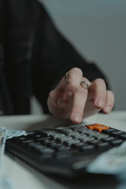 A person's hand with rings presses keys on a calculator in a focused setting.
