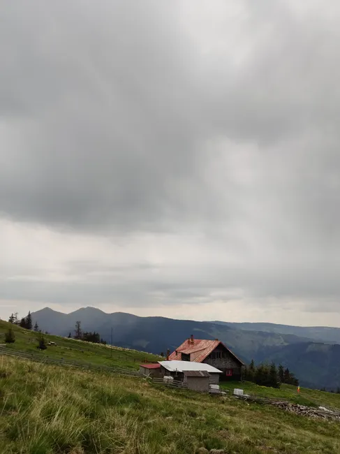 A scenic view of a rural house on mountainous terrain with an overcast sky.
