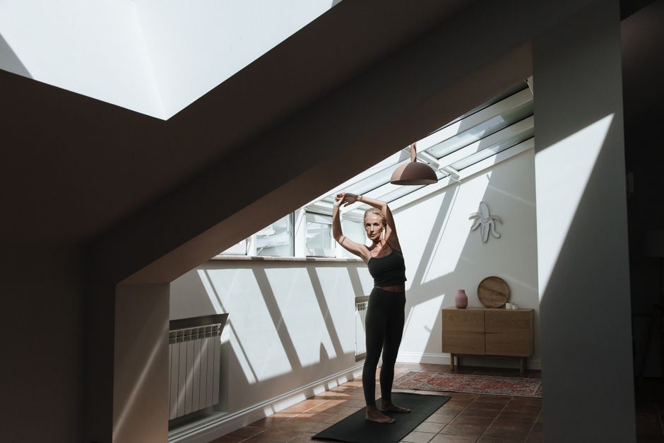A senior woman performs stretching exercises in a sunlit attic room, embracing fitness and health.