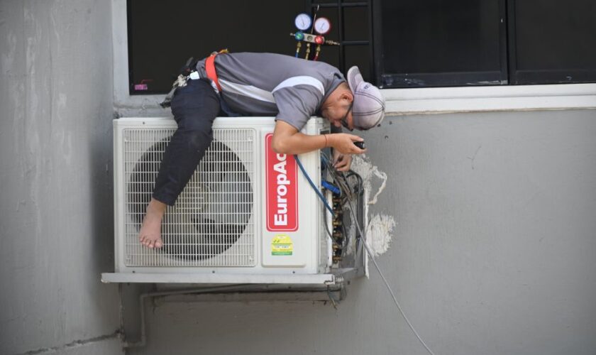 A technician skillfully repairing an outdoor air conditioning unit mounted on a building wall.