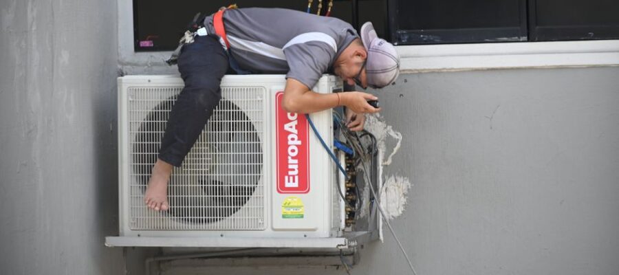 A technician skillfully repairing an outdoor air conditioning unit mounted on a building wall.