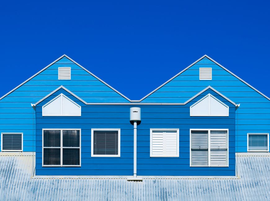 A vibrant blue house facade with windows and a clear sky, showcasing modern architecture.