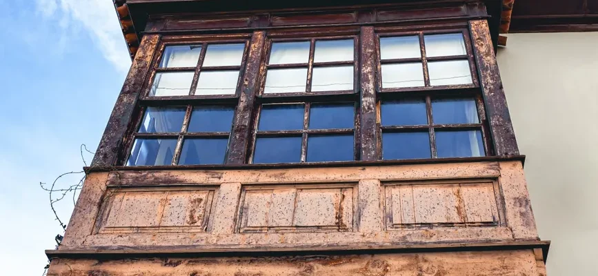 A vintage wooden balcony featuring rustic windows under a clear blue sky.