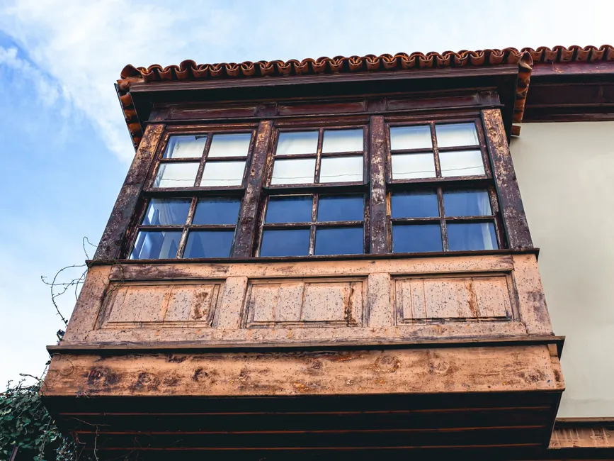 A vintage wooden balcony featuring rustic windows under a clear blue sky.