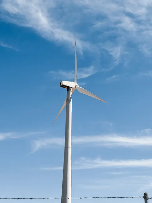 A wind turbine stands tall against a bright blue sky, symbolizing clean energy.
