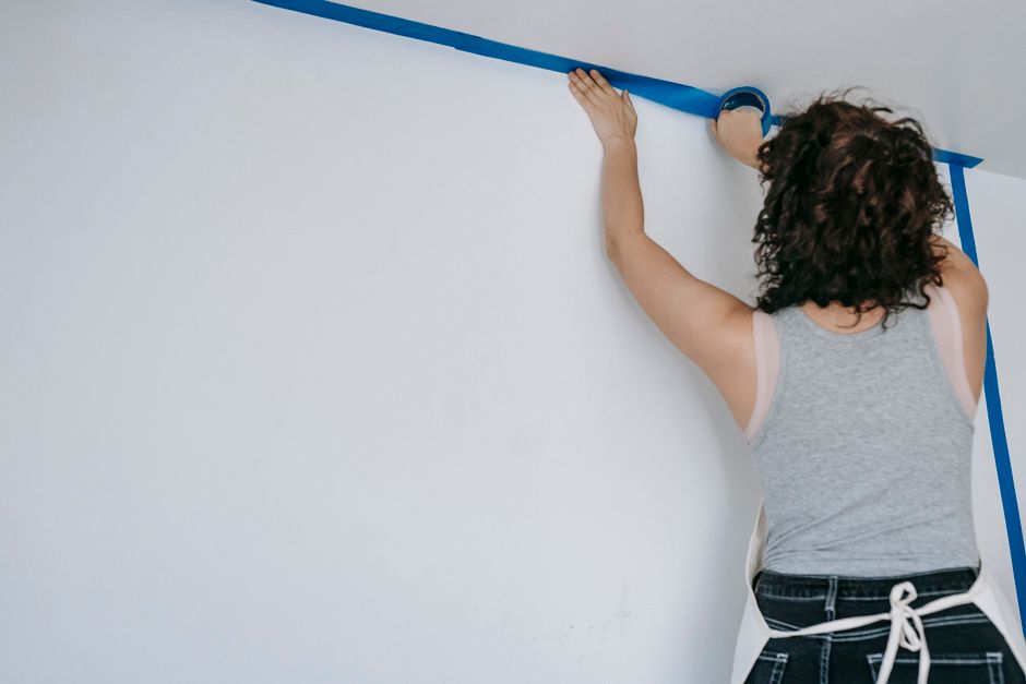 A woman uses painter's tape to prepare a wall for a home renovation project.