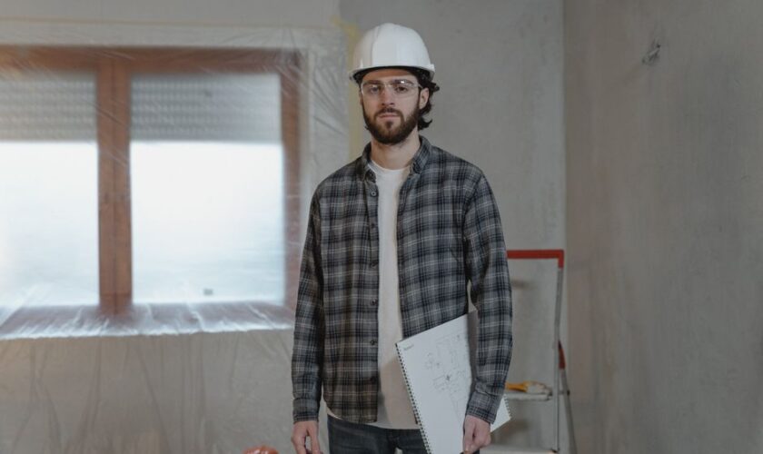 Adult male construction worker holding blueprints in an indoor renovation site.