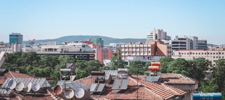 Aerial cityscape of Gaziantep, Turkey, showcasing urban rooftops with solar panels under a bright summer sky.