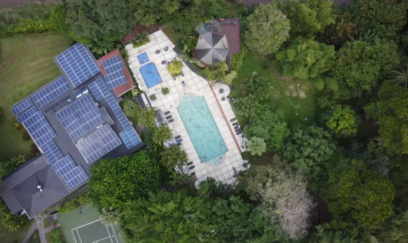 Aerial view of a luxury villa with solar panels and a pool in vibrant green surroundings.