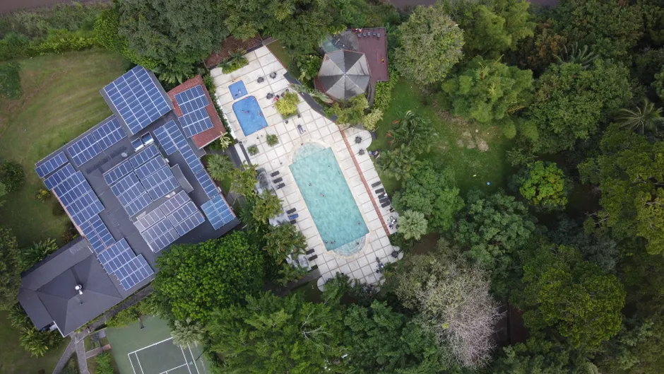 Aerial view of a luxury villa with solar panels and a pool in vibrant green surroundings.