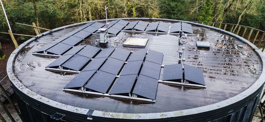 Aerial view of a round rooftop with solar panels surrounded by trees, promoting renewable energy.