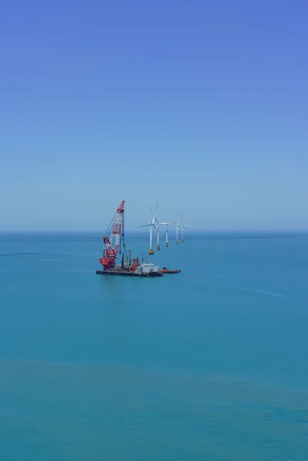 Aerial view of offshore wind turbines being installed in the clear blue sea.