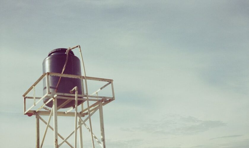 An industrial water tank atop a metal frame against a clear sky, showcasing infrastructure design.