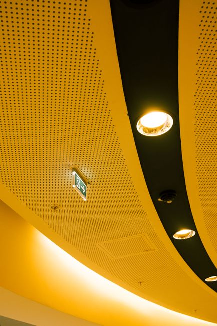 Artistic view of a perforated ceiling with recessed lighting and an exit sign.