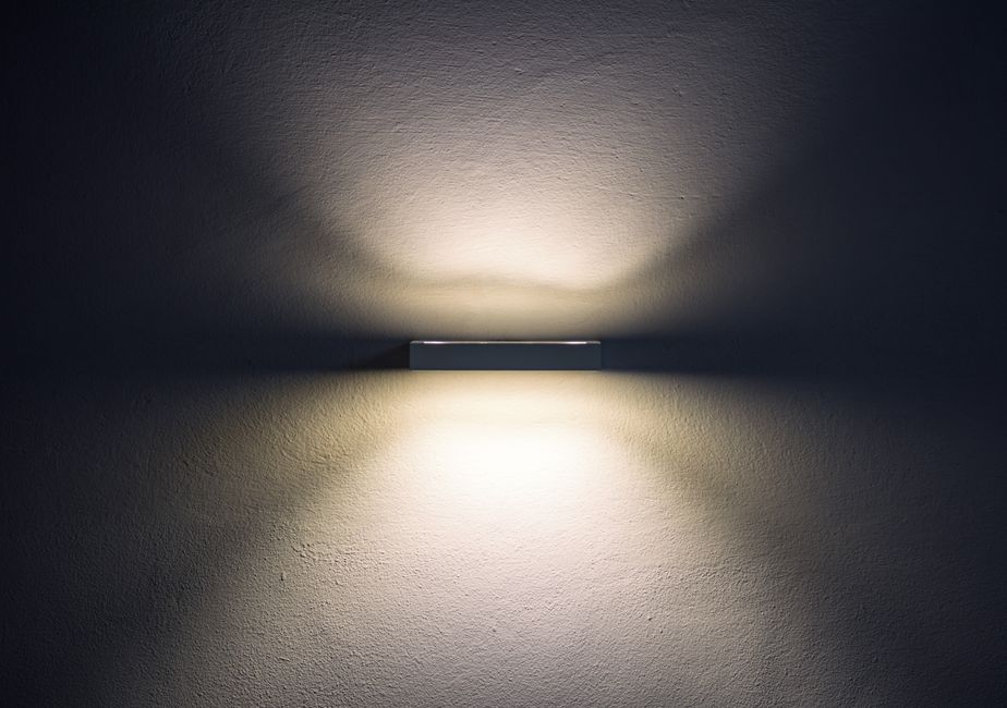 Artistic wall lamp casting soft shadows, creating a minimalist ambiance in a dim setting.