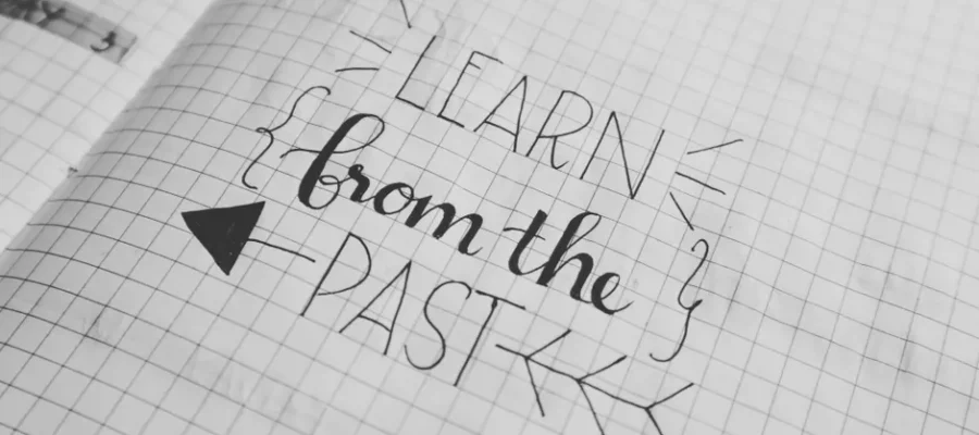 Black and white close-up of a handwritten motivational quote 'Learn from the Past' on graph notebook paper.