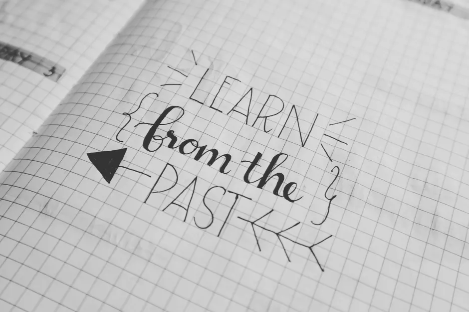 Black and white close-up of a handwritten motivational quote 'Learn from the Past' on graph notebook paper.