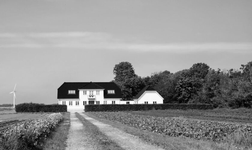 Black and white photo of a secluded country house in Denmark with surrounding fields and a wind turbine.