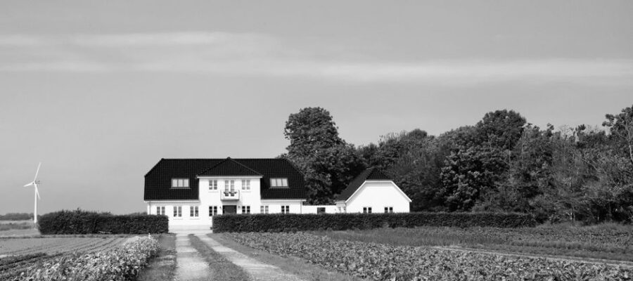Black and white photo of a secluded country house in Denmark with surrounding fields and a wind turbine.