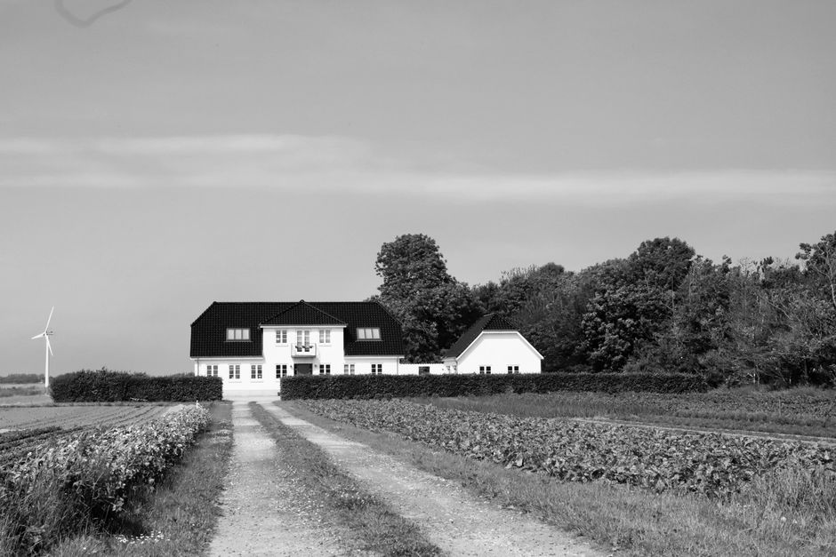 Black and white photo of a secluded country house in Denmark with surrounding fields and a wind turbine.