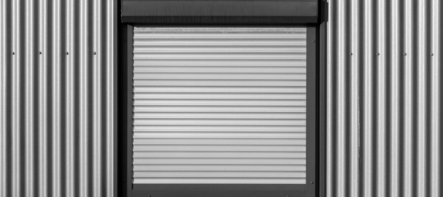 Black and white photo of a window with roller shutter on a corrugated metal wall, showcasing modern architecture.