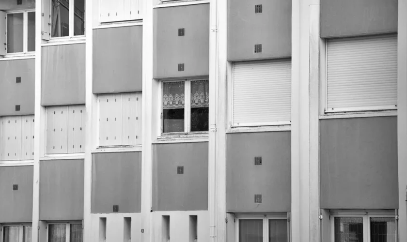 Black and white photo of apartment facade with repetitive window pattern.