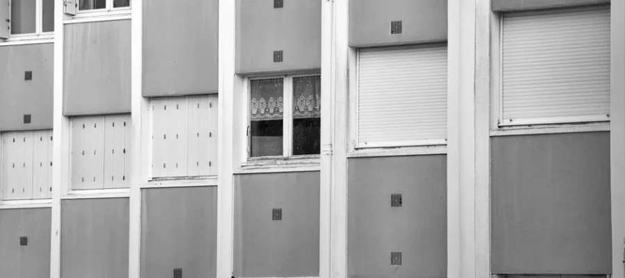 Black and white photo of apartment facade with repetitive window pattern.