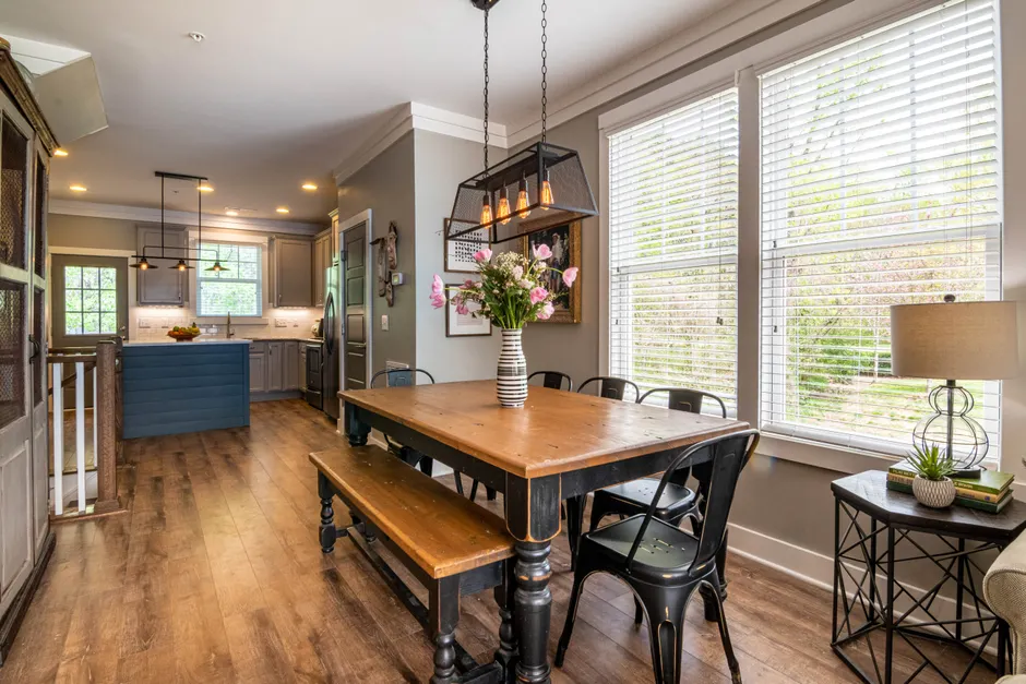 Bright dining area with a rustic table and modern decor, featuring large windows and wooden floors.