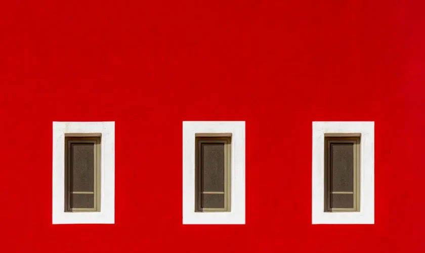 Bright red wall featuring three symmetrically arranged windows with white frames.