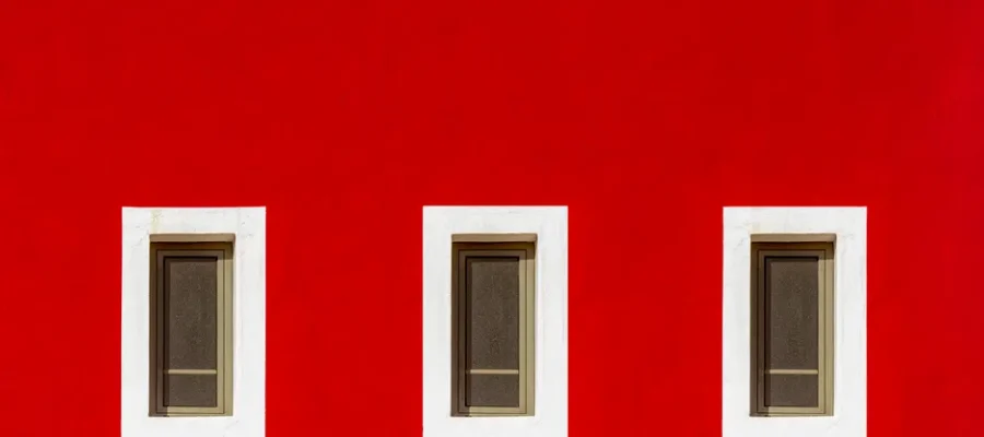 Bright red wall featuring three symmetrically arranged windows with white frames.