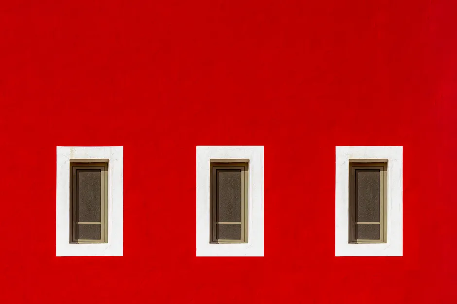Bright red wall featuring three symmetrically arranged windows with white frames.
