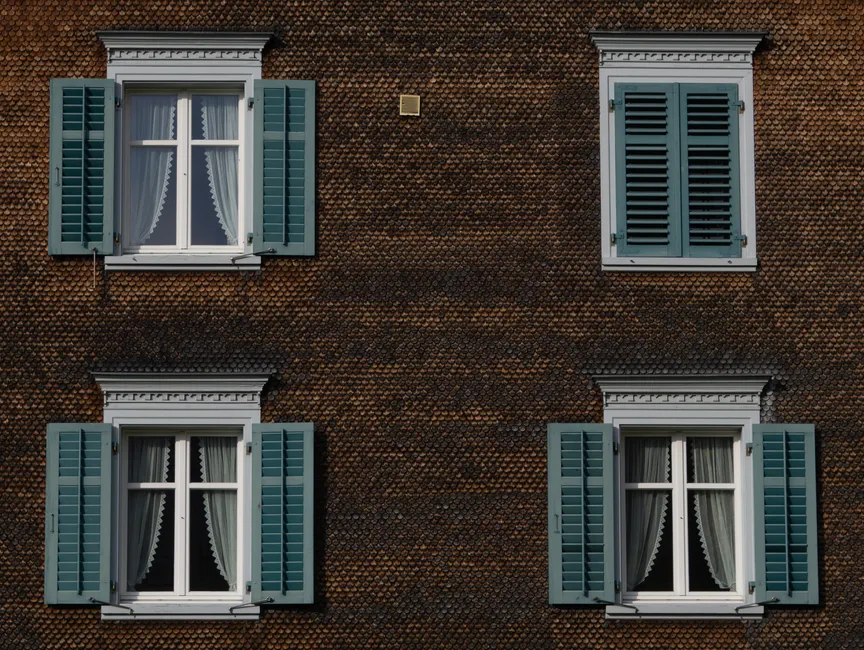 Close-up of a brown building exterior featuring green window shutters and curtains.