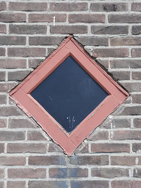 Close-up of a diamond-shaped window on a rugged brick wall, showcasing architectural detail.
