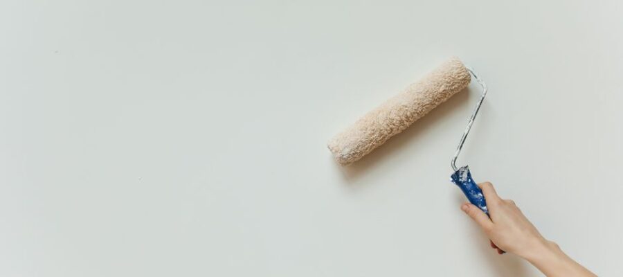 Close-up of a hand painting a wall with a roller brush during renovation.