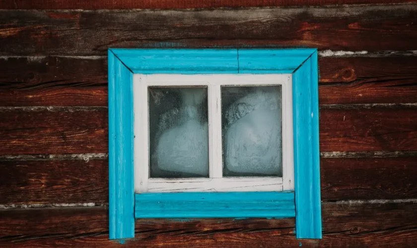 Close-up of a rustic wooden wall with a weathered blue-framed window.