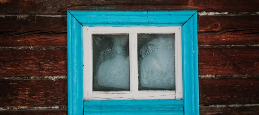 Close-up of a rustic wooden wall with a weathered blue-framed window.